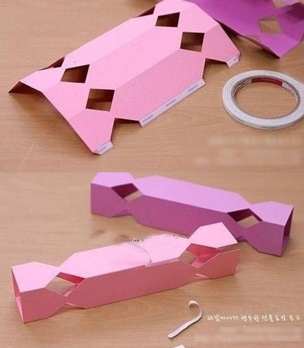 Bước 3. Bạn gấp giấy theo các đường kẻ để tạo nếp cho chiếc hộp. Bạn dán băng dính 2 mặt dọc theo mép giấy ở phần thân và cả hai đầu viên kẹo nữa.Sau đó, bạn dán hai mép giấy với nhau để tạo thành hình viên kẹo.


