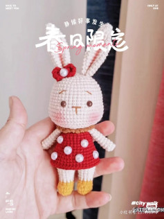 crochet pattern white rabbit with long ears wearing a red dress with white dots, tied with a red bow.