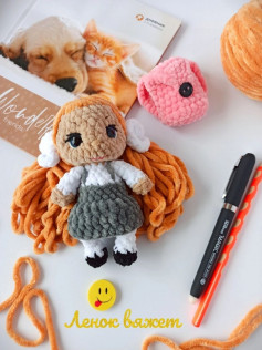 Вязаная крючком кукла с оранжевыми волосами в сером комбинезоне.