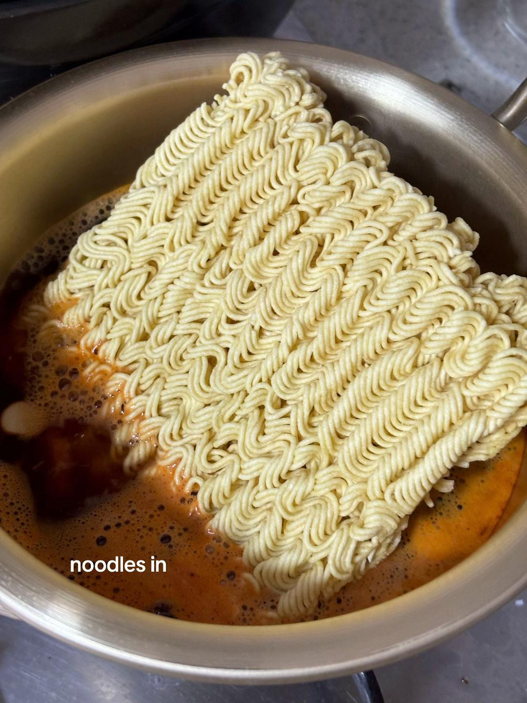 Cooking Nongshim Yukgaejang Ramyeon with kimchi and vegetables in a brass pot