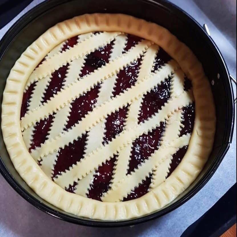 Crostata di pasta frolla con marmellata di albicocche e ciliegie decorata a fiore e intreccio
