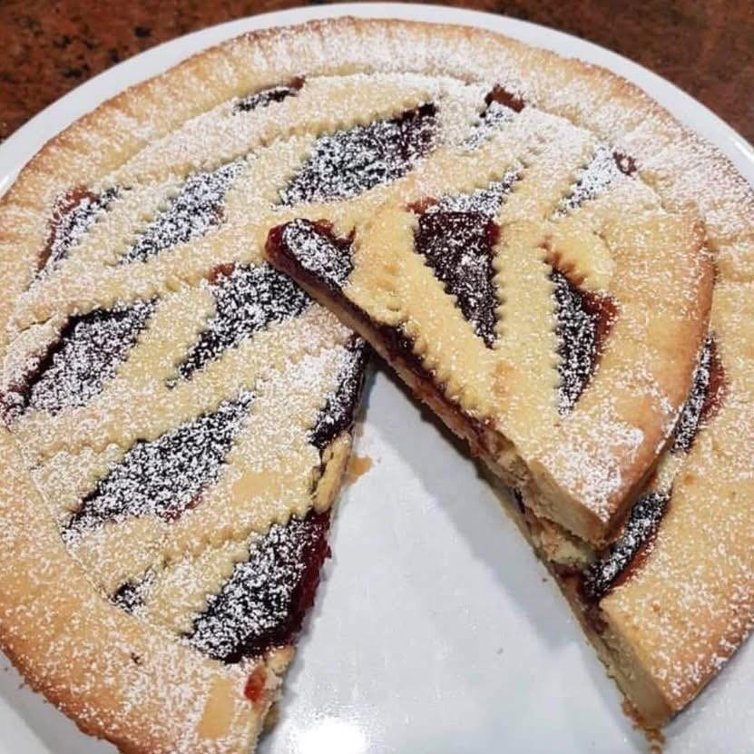 Crostata di pasta frolla con marmellata di albicocche e ciliegie decorata a fiore e intreccio