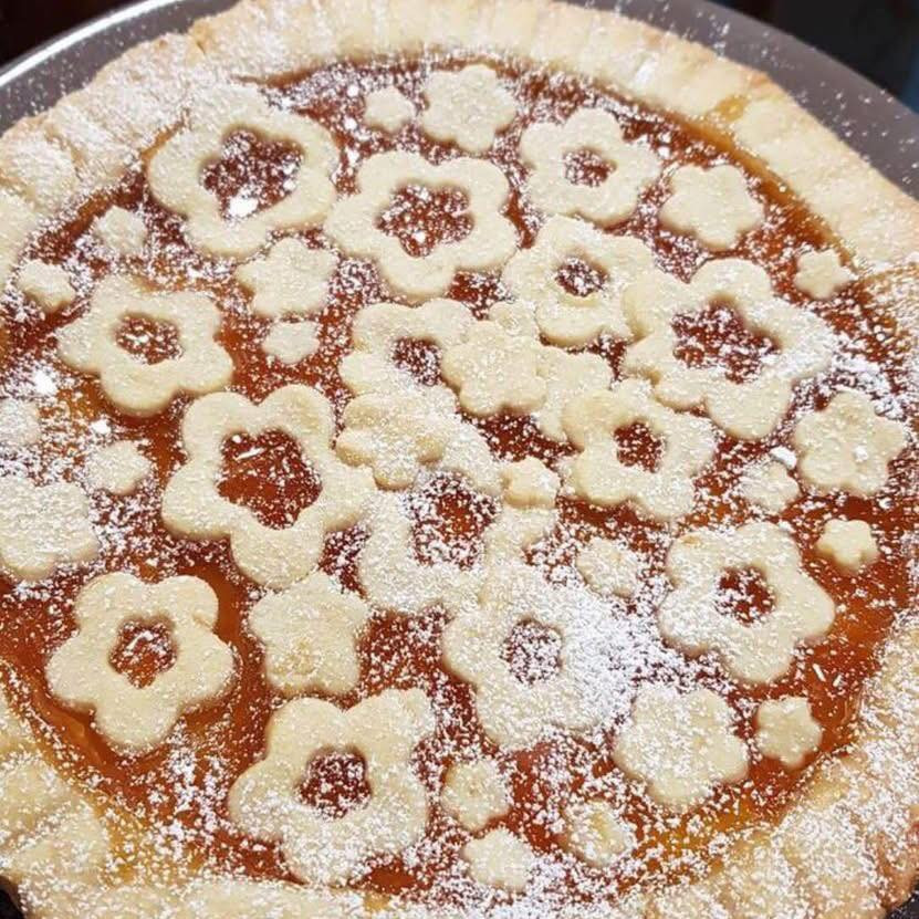 Crostata di pasta frolla con marmellata di albicocche e ciliegie decorata a fiore e intreccio