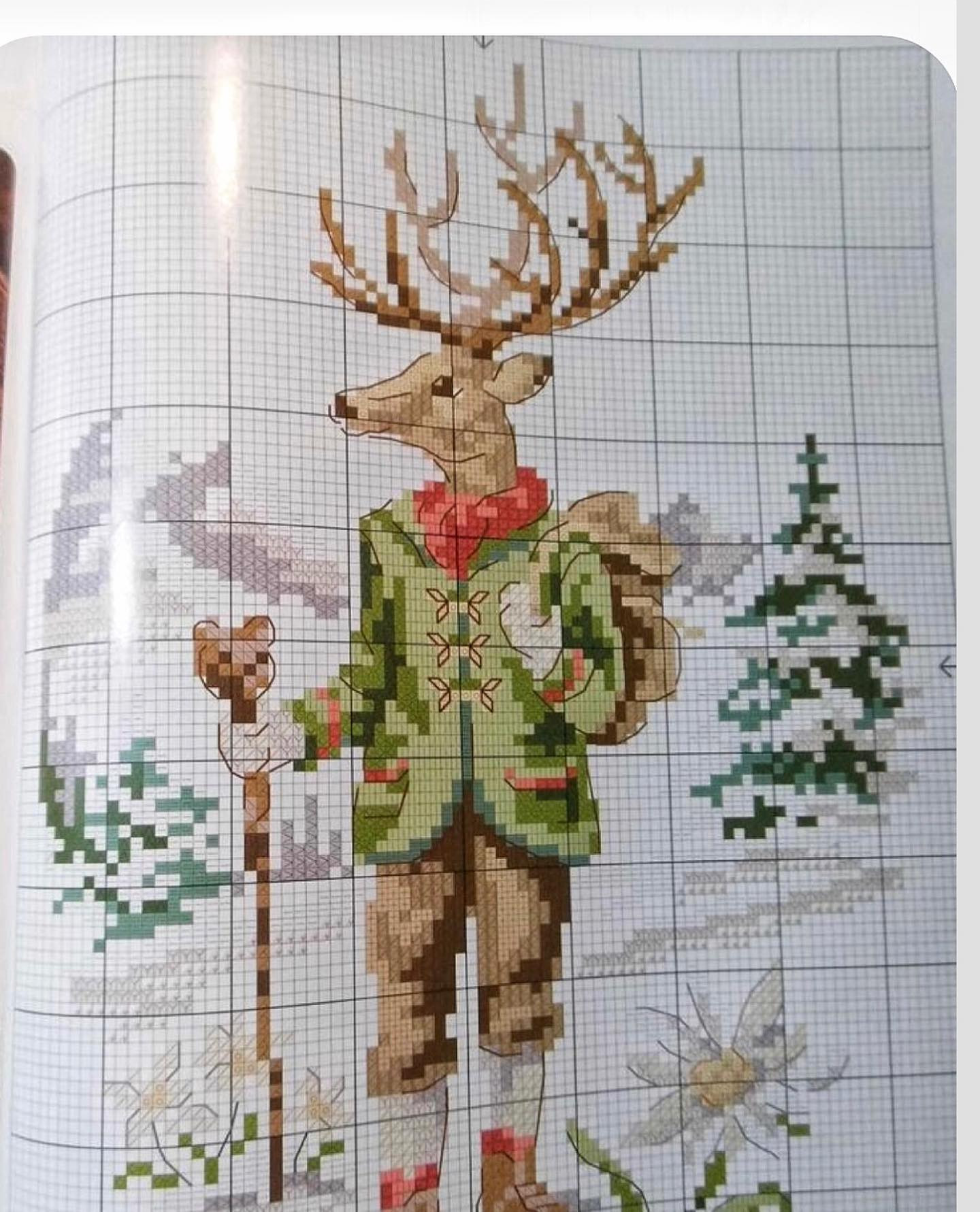 Pixel chart pattern of a cute anthropomorphic deer character wearing green jacket, red scarf and carrying backpack in winter forest