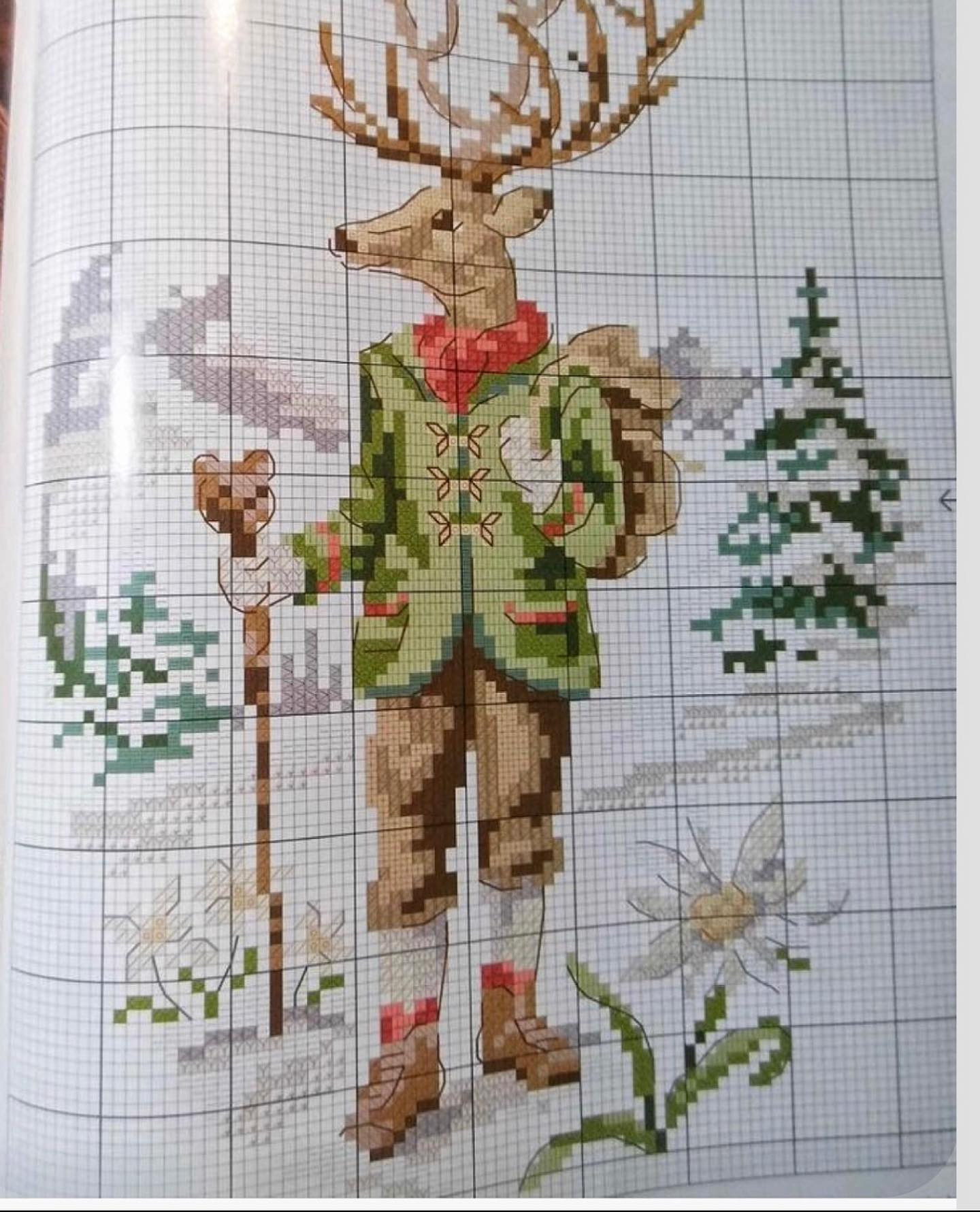 Pixel chart pattern of a cute anthropomorphic deer character wearing green jacket, red scarf and carrying backpack in winter forest